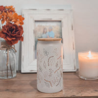 Frosted Glass tumbler with fall illustrations on a table next to a candle and flowers, with a blurred photo frame in the background.
