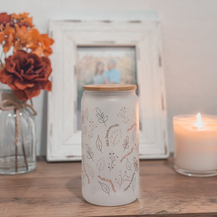 Frosted Glass tumbler with fall illustrations on a table next to a candle and flowers, with a blurred photo frame in the background.
