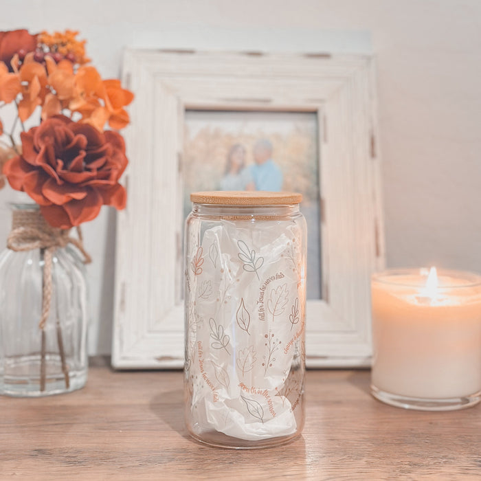 Clear Glass tumbler with fall illustrations on a table next to a candle and flowers, with a blurred photo frame in the background.