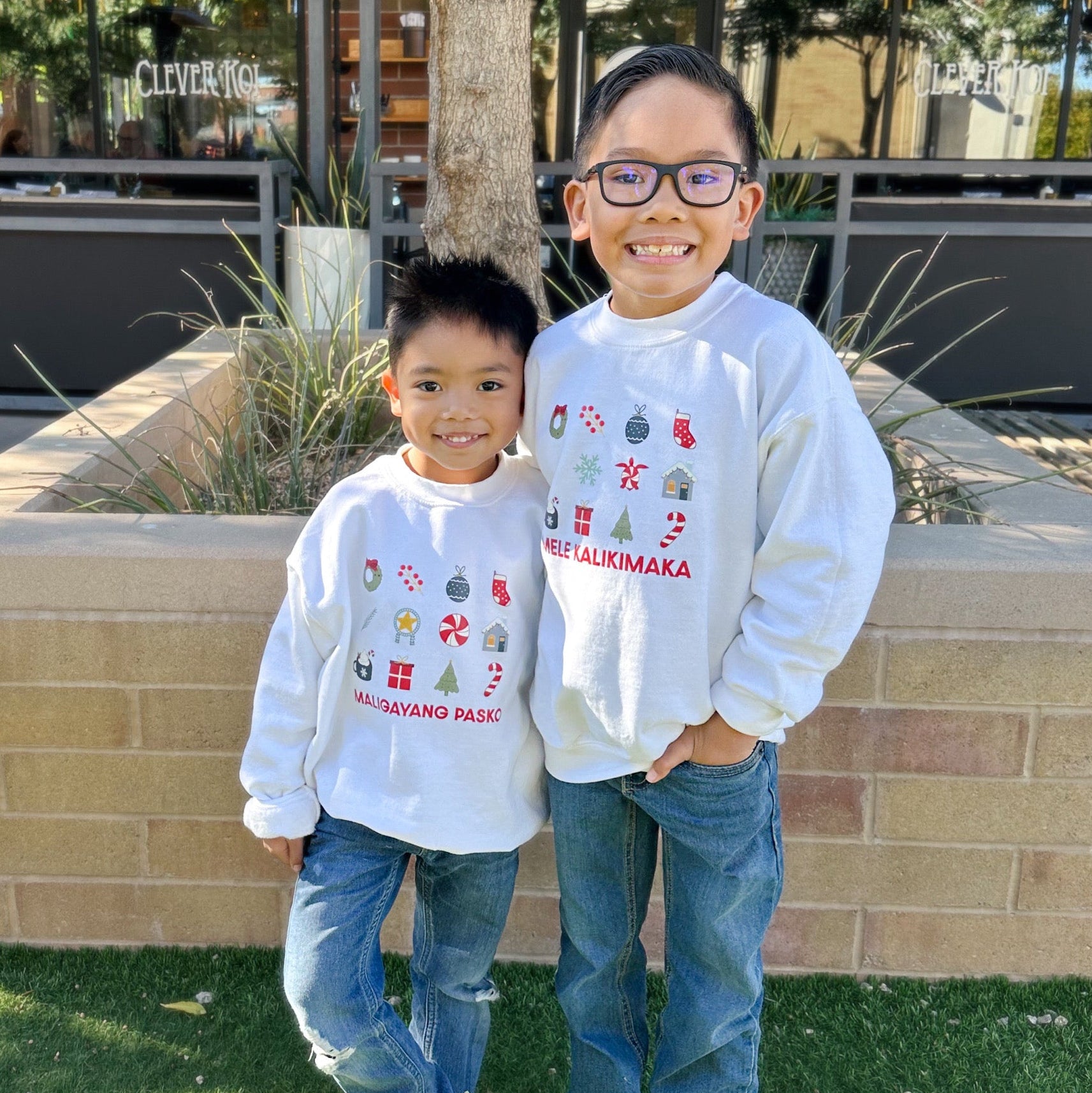 Two children wearing matching sweatshirts standing outdoors on a sunny day.